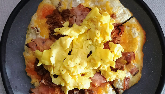 Scrambled eggs with bacon and ham on cheesy flatbread from the Breakfast Menu at Cosmic Golf.