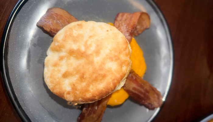 Biscuit sandwich with bacon and melted cheese from the Breakfast & Brunch Menu at Cosmic Golf.